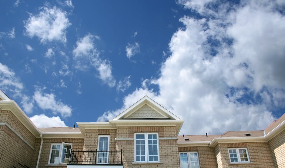 A modern brick house with large windows set against a bright blue sky with fluffy clouds